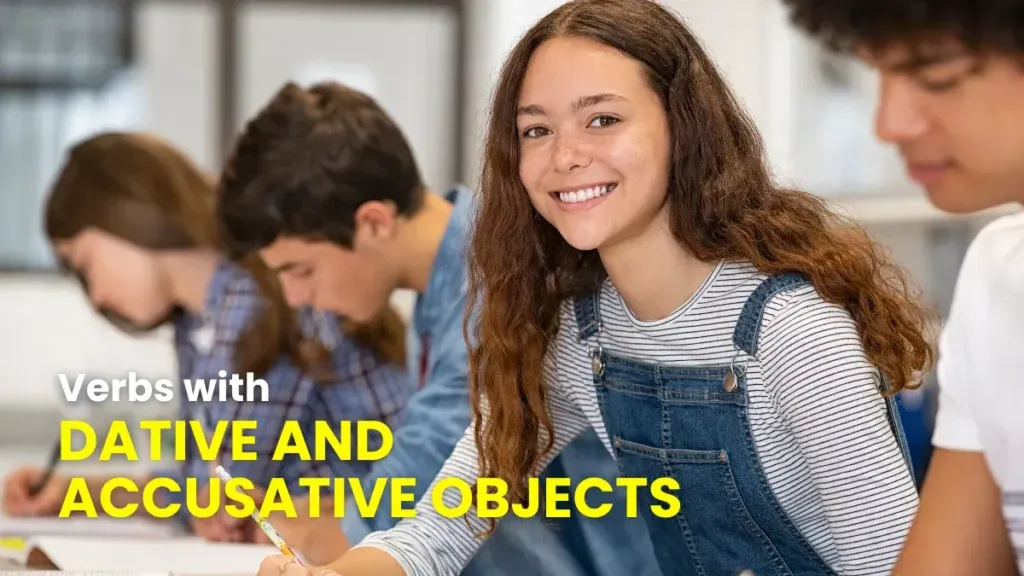 Group of young students writing in notebooks at a desk, smiling and learning about verbs with dative and accusative objects in German.